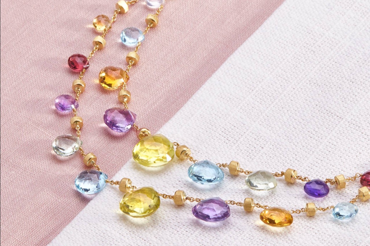 close up image of a yellow gold necklace with featuring multiple different gemstones