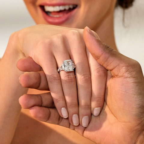 A man holding a woman’s hand with a close-up of a large center stone diamond ring and her smile in the background.